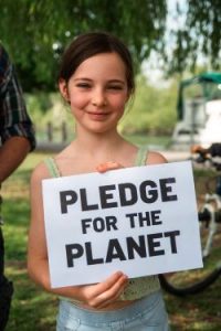 A young girl smiling holds up a sign saying "pledge for the planet"