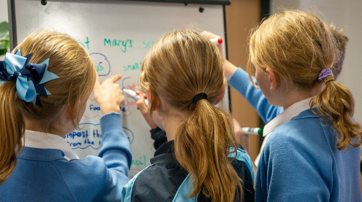 Three girls from St Mary's School write ideas on a whiteboard