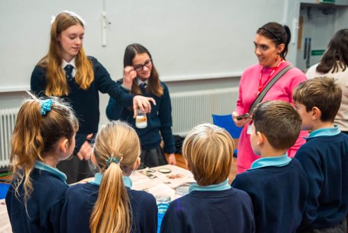 Older children show primary school children a science experiment at the Schools Environmental Challenge. A teacher looks on smiling