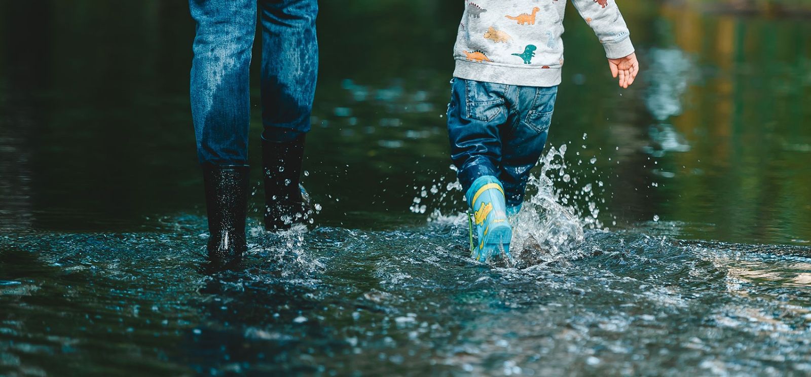 An image of a mother and daughter splashing through a flood with wellies on