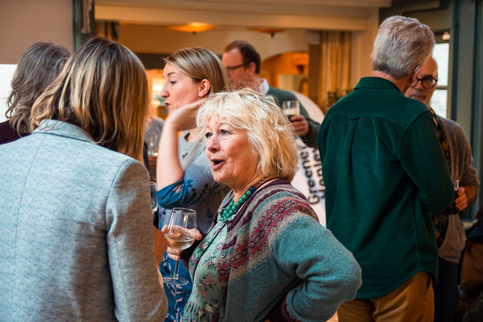 a group of people chatting in a pub with a Greener Henley banner in the background