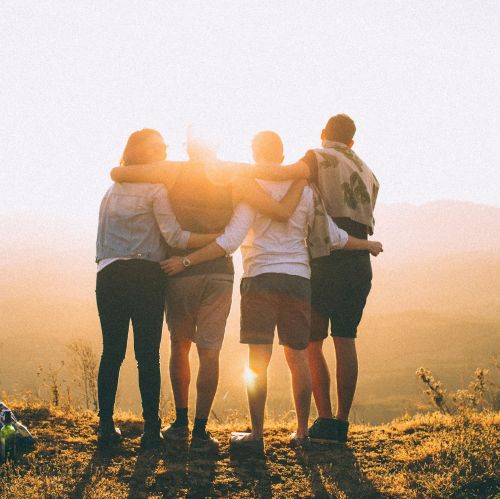 a group of people stand facing the sunset with arms around each other